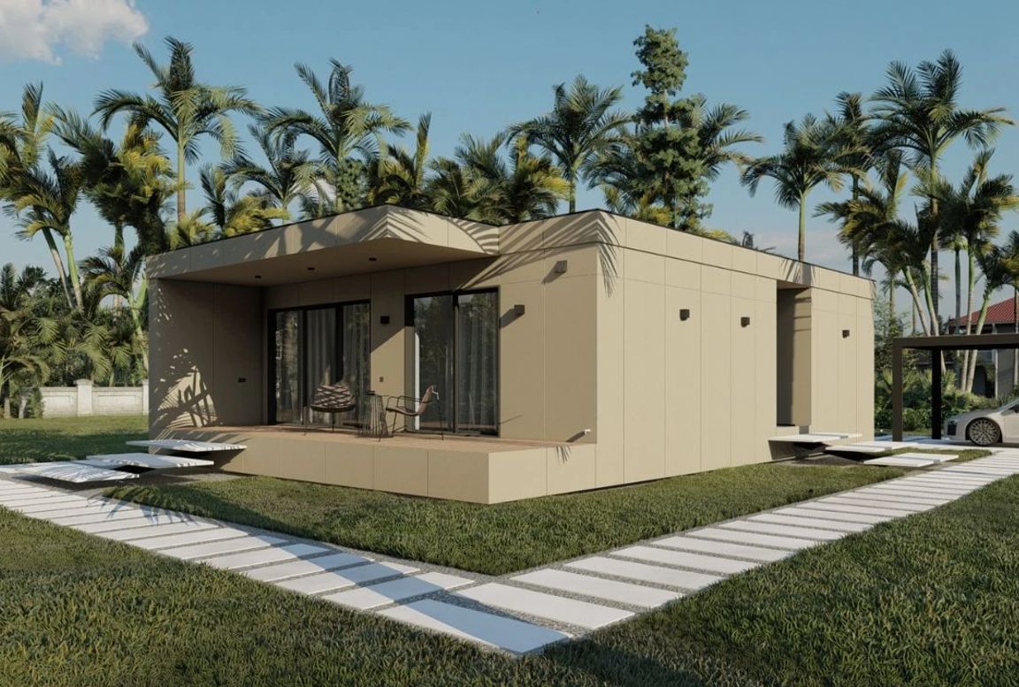 Modern modular home with a beige exterior, featuring a front deck, large sliding glass doors, and a sleek pathway surrounded by palm trees and green lawn.