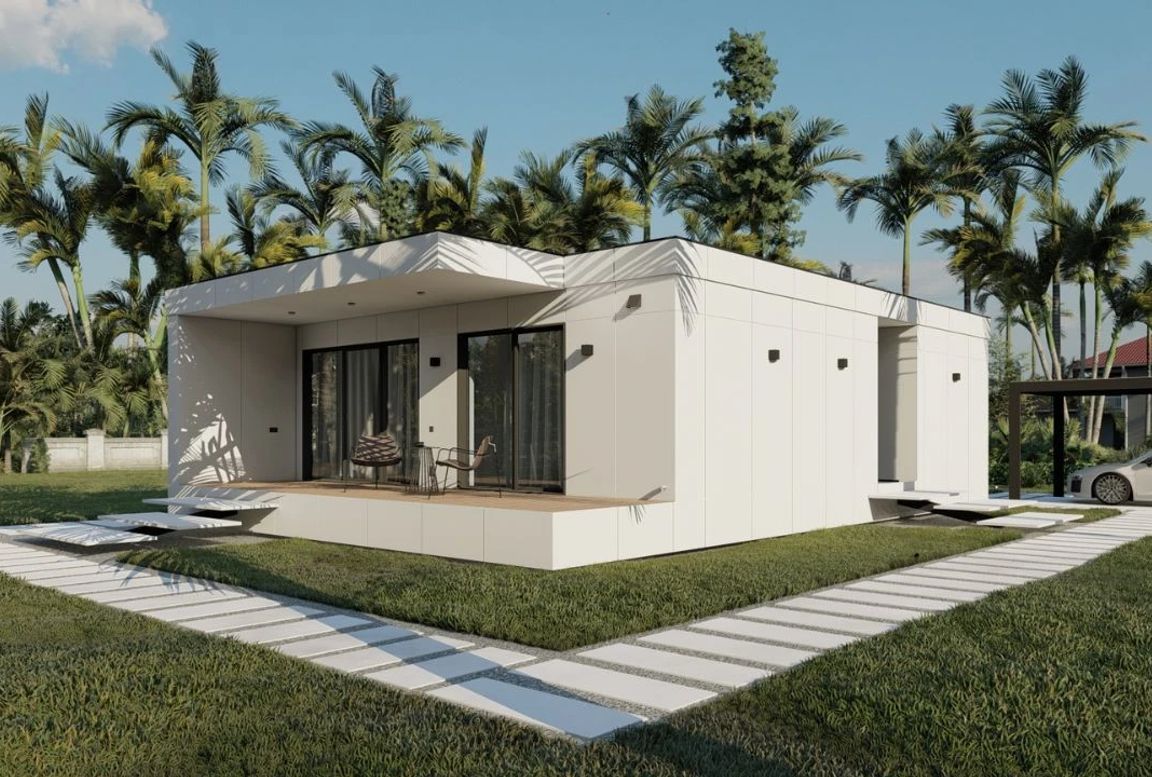 Elegant white modular home with a minimalist design, front porch area, and tropical garden backdrop including palm trees and a parked car in a black-frame carport.