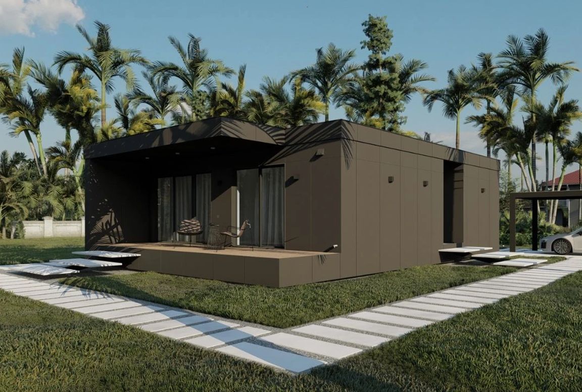 Contemporary two-bedroom modular house in dark brown, showcasing a wooden deck, minimal black lighting fixtures, and tropical landscaping with a carport visible.