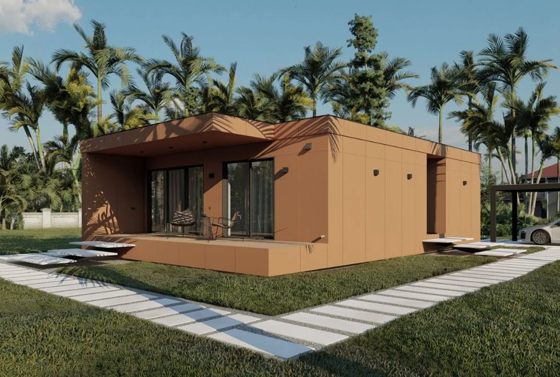 Modern orange-toned modular house with geometric lines, a wooden terrace, and a white stepping-stone walkway, surrounded by grass and palm trees.