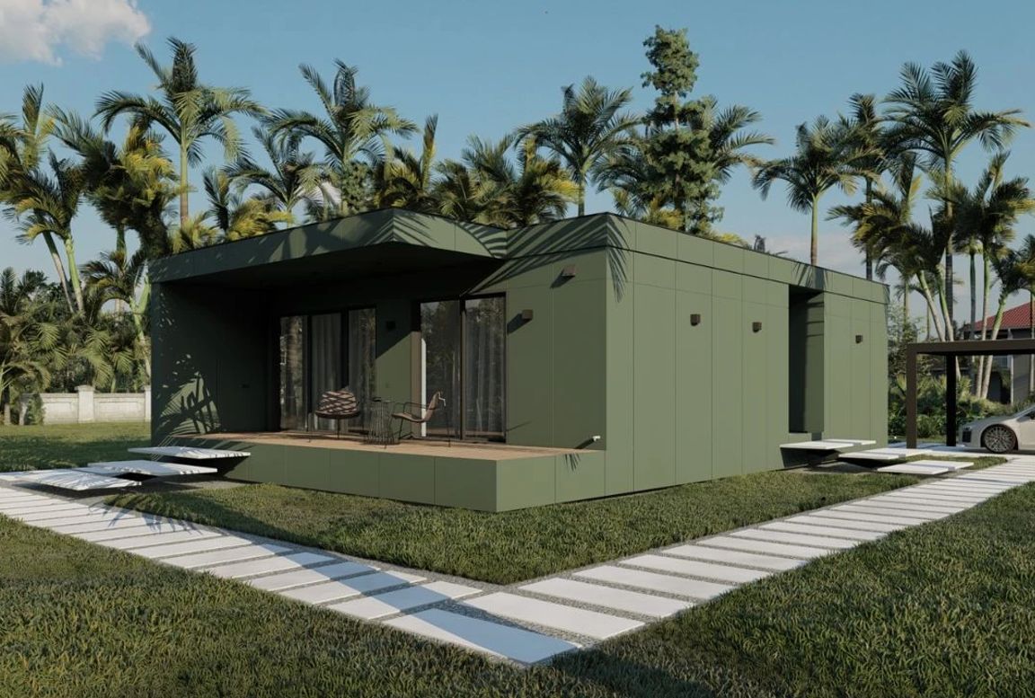 Stylish prefabricated home with a green facade, front-facing patio, and a clean grid-like path, set in a tropical garden with tall palm trees.